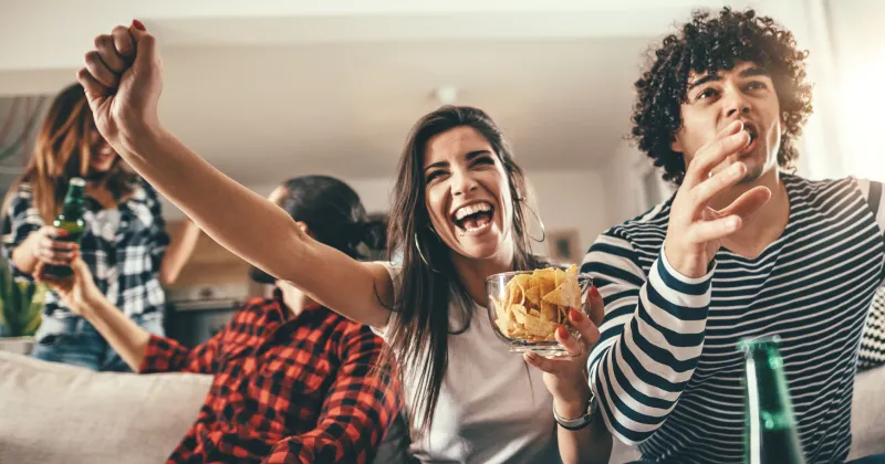 A group of people cheering while eating snacks in a home.