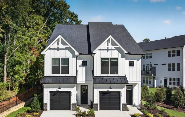 Front elevation of the Harrington End Unit at 613 Cable Court in Parc at Bradley Farm, featuring white board-and-batten siding, black metal roof accents, a black front door and a one-car garage.