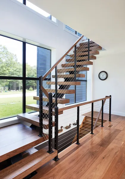 Custom walnut floating staircase with wire railings in front of a window feature wall.