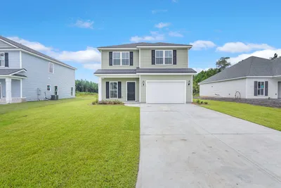 Hatteras A two-story exterior with light green siding, dark shutters, a hip roof, a covered front porch, and an attached garage.