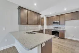 Hatteras kitchen with dark gray cabinets, white countertops, a breakfast bar, stainless steel appliances, and a view into the optional butler’s pantry / coffee bar.