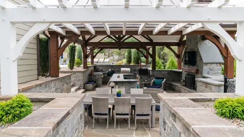 Patio with stone walls and a pergola with a grill inside from garman builders