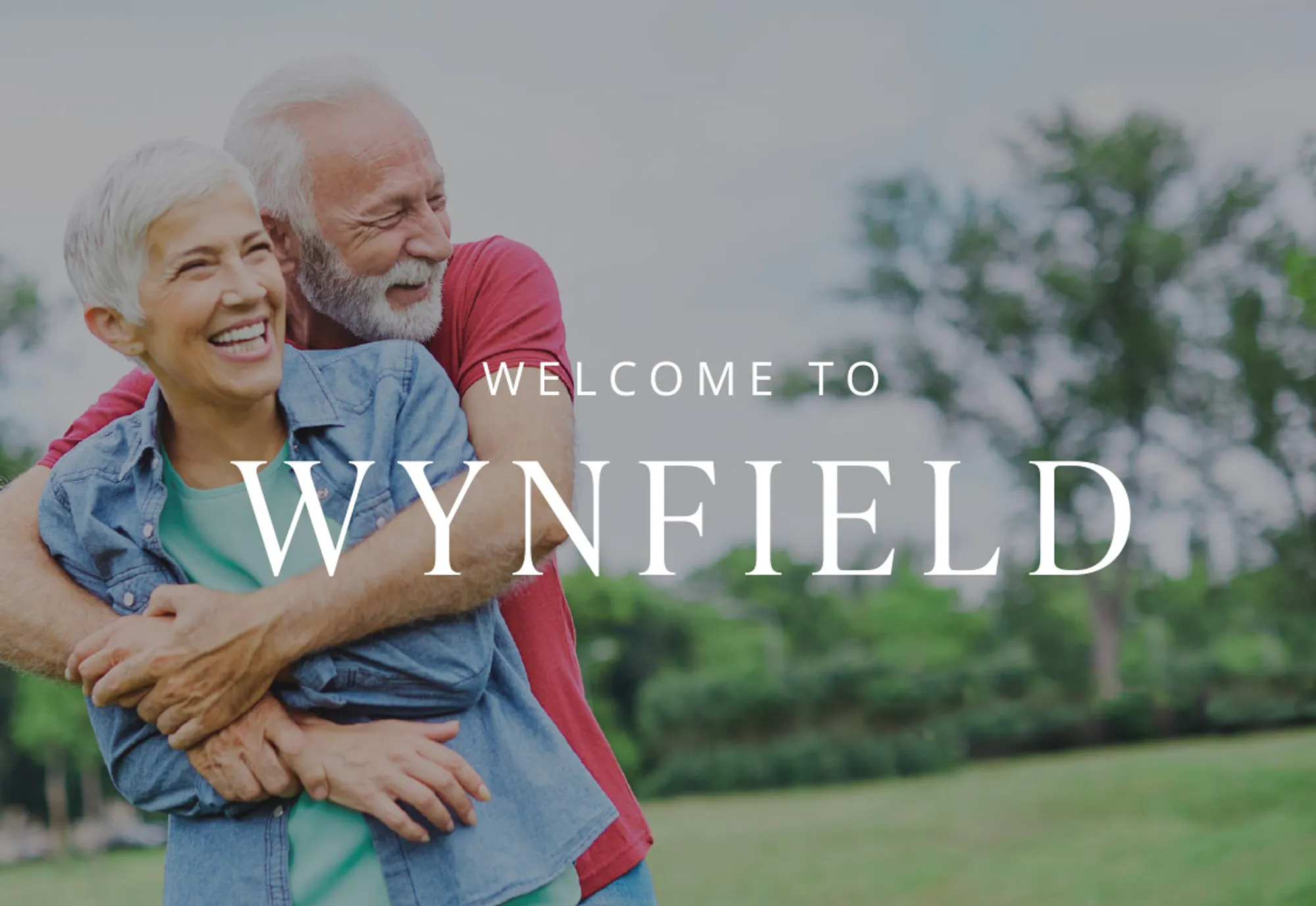 Two active adults hugging in a park with the words "Welcome to Wynfield" written in front of them