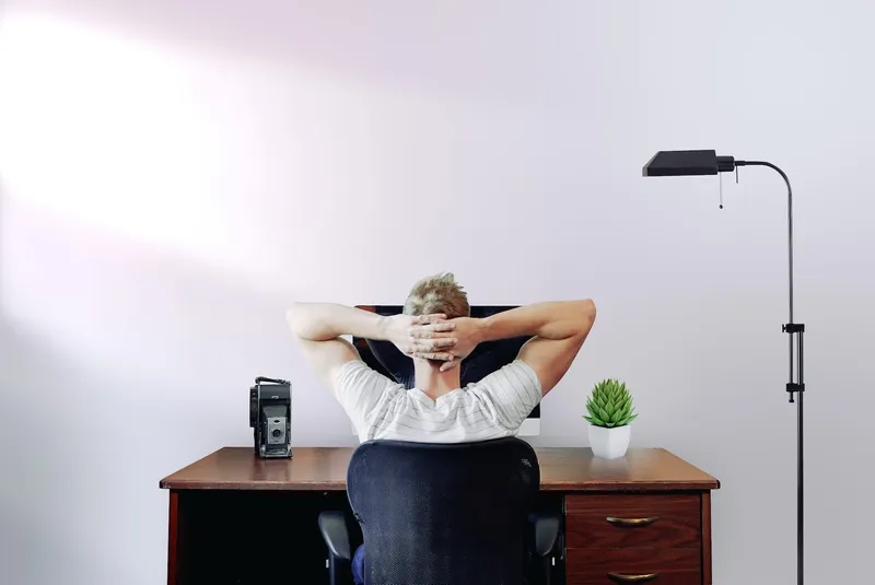 Man Sitting in his home office with hands behind his head