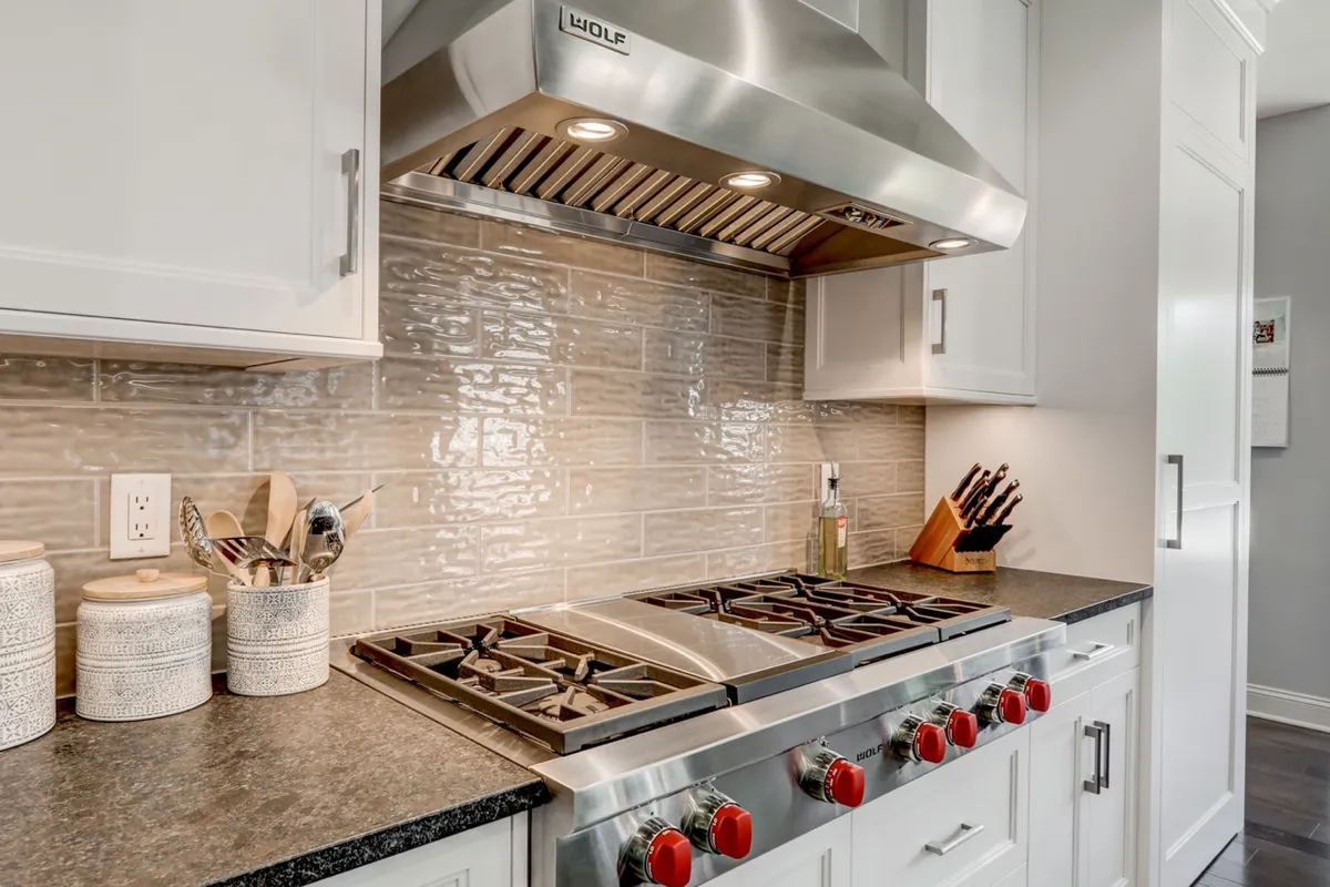 high-end stove and gas cooktop with stainless steel hood, white cabinets and tile backsplash