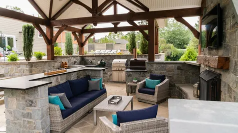 Patio with stone walls and a pergola with a grill inside from garman builders