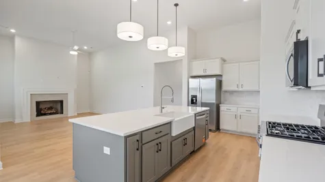 Spacious kitchen island with an undermount farmhouse sink, light wood-finish flooring, and stainless steel appliances, including a range and refrigerator