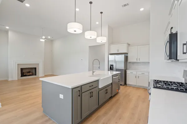 Spacious kitchen island with an undermount farmhouse sink, light wood-finish flooring, and stainless steel appliances, including a range and refrigerator