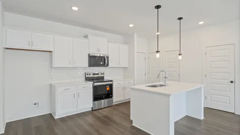 Modern kitchen featuring white cabinetry, subway tile backsplash, stainless steel appliances, and a central island with a sink and pendant lighting
