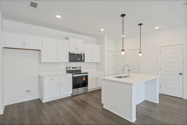 Modern kitchen featuring white cabinetry, subway tile backsplash, stainless steel appliances, and a central island with a sink and pendant lighting