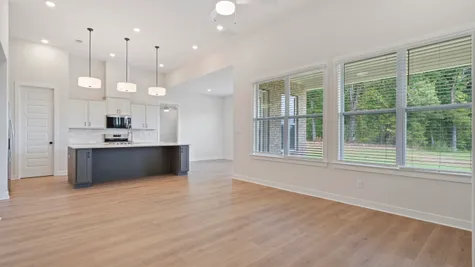 Open-concept living space featuring wood-finish flooring, a kitchen island with seating, stainless steel appliances, and abundant natural light from multiple windows