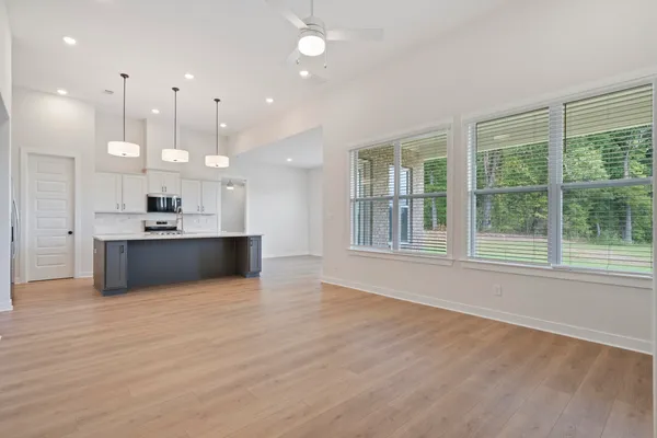 Open-concept living space featuring wood-finish flooring, a kitchen island with seating, stainless steel appliances, and abundant natural light from multiple windows