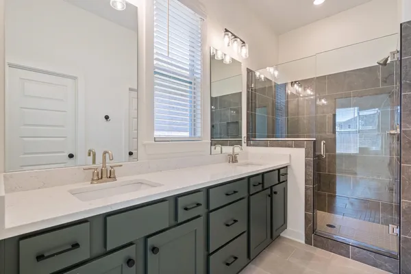 Dual vanity with integrated sinks and brushed nickel faucets, quartz countertop, dark cabinetry with matte black hardware, and a glass-enclosed shower with tiled walls and floor