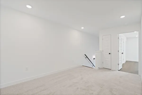 Recessed lighting, light-toned carpeting, white five-panel interior doors, and a black handrail
