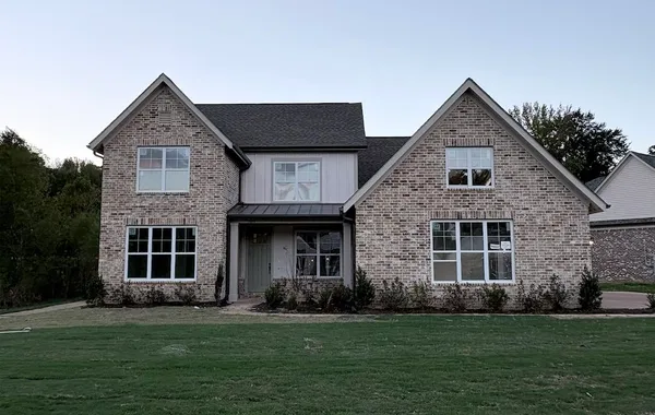Two-story brick exterior featuring double gables, vertical siding accents, and a metal roof portico