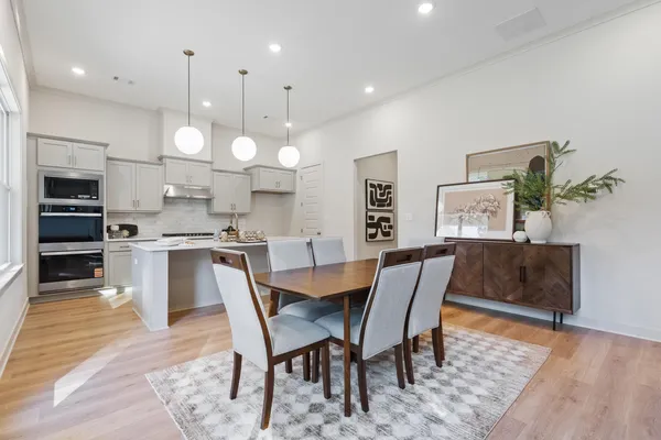 Kitchen featuring a central island, light-toned cabinetry, built-in double ovens, and three pendant lights, complemented by wood-finish flooring