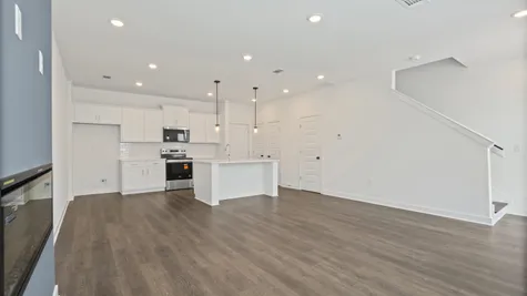 Open concept living space featuring wood-finish flooring, recessed lighting, and a modern kitchen with white cabinetry and stainless steel appliances