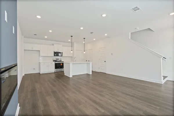 Open concept living space featuring wood-finish flooring, recessed lighting, and a modern kitchen with white cabinetry and stainless steel appliances