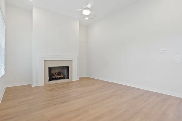 Spacious room featuring vaulted ceilings, wood-finish flooring, a fireplace with a stone surround, recessed lighting, and a ceiling fan