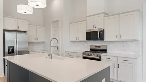 Open-concept kitchen featuring an expansive island with an undermount sink, white shaker cabinetry, stainless steel appliances, and a tile backsplash