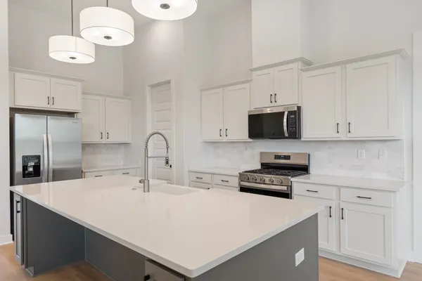 Open-concept kitchen featuring an expansive island with an undermount sink, white shaker cabinetry, stainless steel appliances, and a tile backsplash