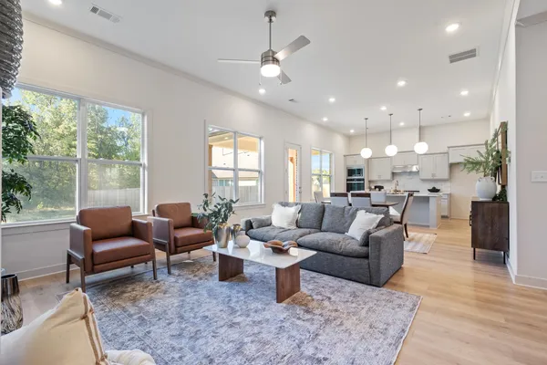 Open-concept living space featuring wood-finish flooring, recessed lighting, a modern ceiling fan, and large windows