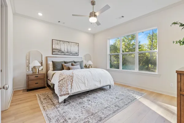 Neutral walls, wood-finish flooring, crown molding, brushed nickel ceiling fan with integrated lighting, and oversized multi-pane windows