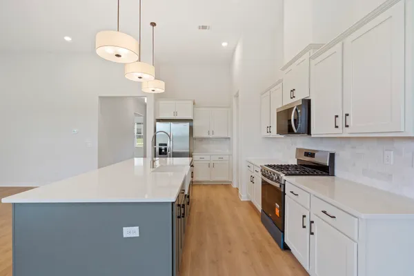 Kitchen featuring a large central island, white cabinetry with dark hardware, stainless steel appliances, and wood-finish flooring