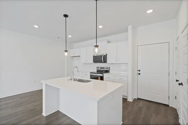 Kitchen with white cabinetry, stainless steel appliances, a subway tile backsplash, and a central island with a sink and pendant lighting