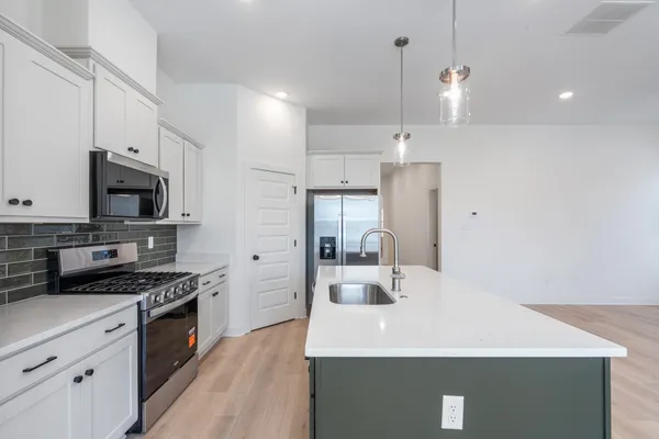 Kitchen featuring white shaker cabinetry, stainless steel appliances, dark subway tile backsplash, and an island with a stainless steel sink