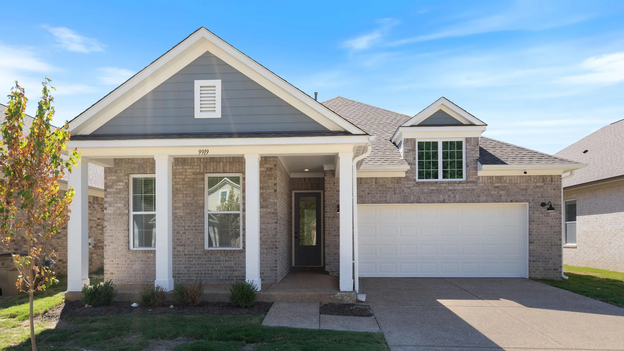 Brick exterior with gray siding accents, covered front porch, white garage door, and a dormer window