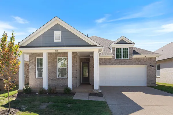 Brick exterior with gray siding accents, covered front porch, white garage door, and a dormer window