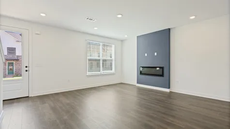 Recessed lighting, wood-finish flooring, a contemporary accent wall, an integrated fireplace, and a glass-paneled door
