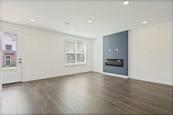 Recessed lighting, wood-finish flooring, a contemporary accent wall, an integrated fireplace, and a glass-paneled door
