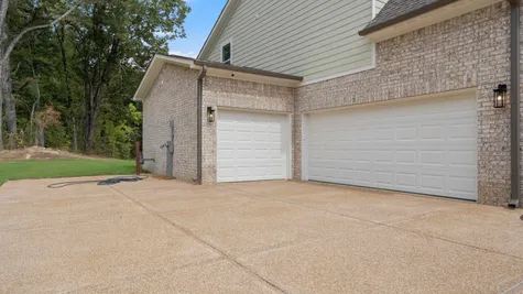 Brick exterior with light-colored siding, two white garage doors, and an exposed aggregate driveway