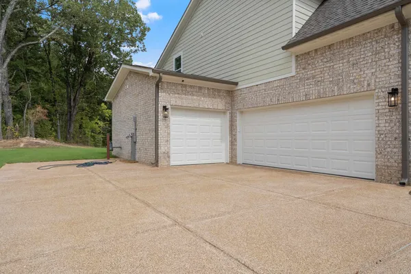 Brick exterior with light-colored siding, two white garage doors, and an exposed aggregate driveway