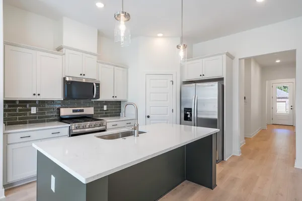 Contemporary kitchen with white cabinetry, a center island with quartz countertop, stainless steel appliances, and a dark green subway tile backsplash