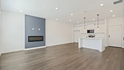 Open-concept living space featuring wood-finish flooring, recessed lighting, and a linear fireplace with an accent wall