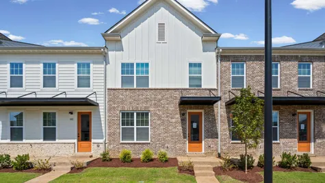 Modern townhome with mixed material facade, brick and horizontal siding, metal awnings, and a concrete walkway