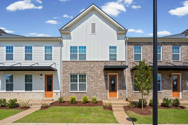 Modern townhome with mixed material facade, brick and horizontal siding, metal awnings, and a concrete walkway