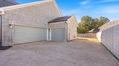 Brick exterior with a three-car garage, concrete driveway, and wooden privacy fencing