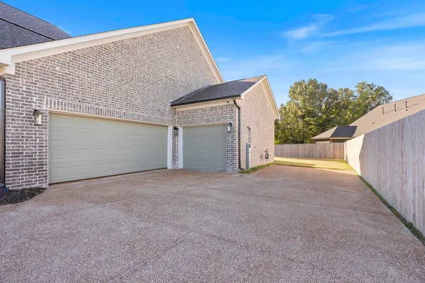 Brick exterior with a three-car garage, concrete driveway, and wooden privacy fencing