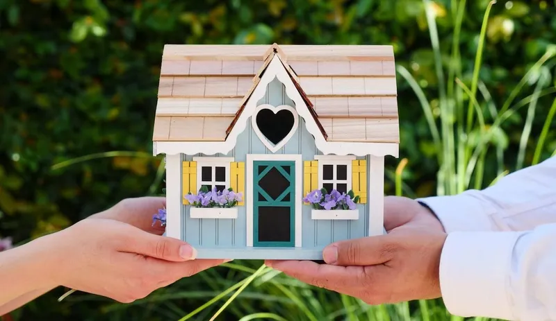 People Holding a Small Model House
