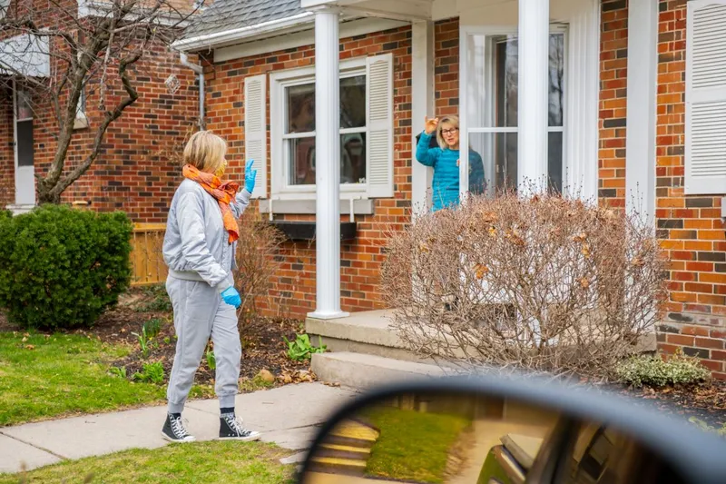 Woman Standing at Her Front Door Waving to Another Woman