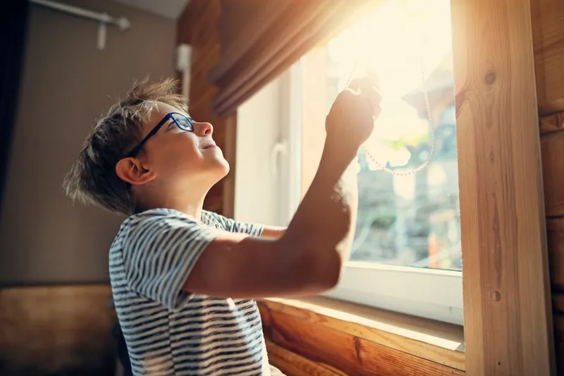 Child opening the blind to a bright sun glare