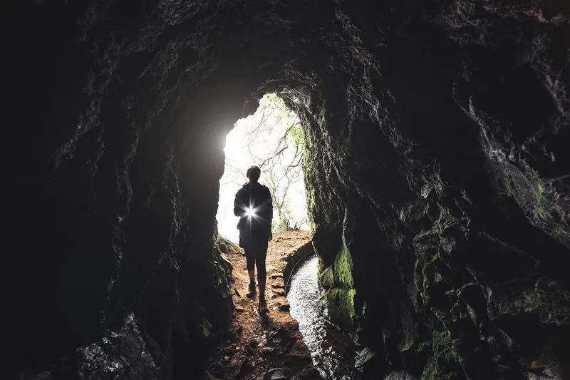 Person Holding a Flashlight Entering a Dark Cave