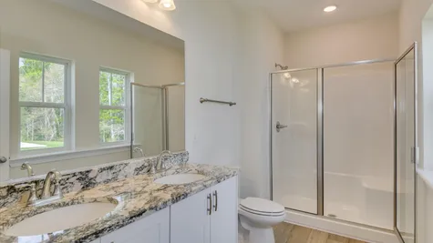 Interior view of the primary bathroom in the newly constructed home by Ivey Homes at 854 Rachel Branch Forrest Bluff, North Augusta, SC 29841, featuring beautiful granite countertops, a dual sink with vanity, and abundant natural light.