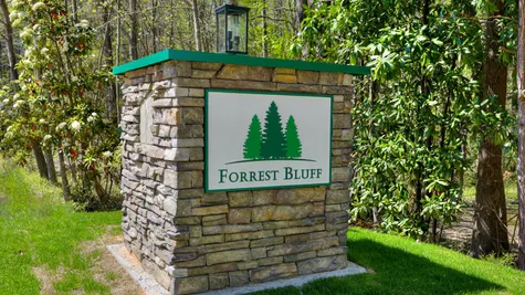 A stonework sign marking the entrance of the Forrest Bluff community by Ivey Homes, surrounded by lush trees in North Augusta, SC.