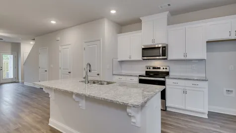 Modern kitchen in a new townhome at 627 Hampton Drive featuring white cabinets, stainless steel appliances, and granite countertops.