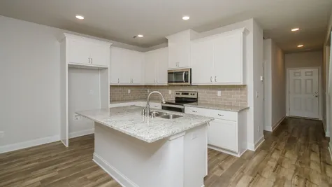 A chic and contemporary kitchen featuring a tile backsplash and granite countertops, part of a new townhome by Ivey Homes located at 1012 Candleberry Drive in Grovetown, GA, with prices starting in the $200s.